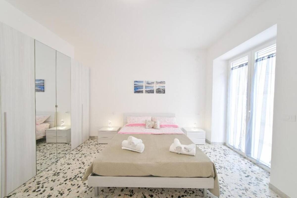 A bedroom with a bed, bedside tables, a large mirror, and a window with curtains.