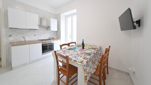 A kitchen with white cabinets, a stove, and a dining table with chairs. - Casa Lulù (Ischia)