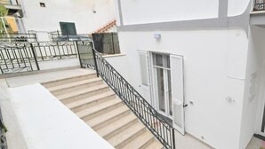 A residential building with a staircase leading to a balcony, white exterior walls, and a metal railing. - Casa Lulù (Ischia)