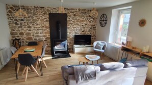 Een gezellige woonkamer met een stenen muur, een open haard, een televisie, een bank en een eethoek met stoelen.