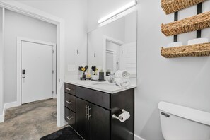 Ein modernes Badezimmer mit einem weißen Waschtisch, einem großen Spiegel und einer Toilette.