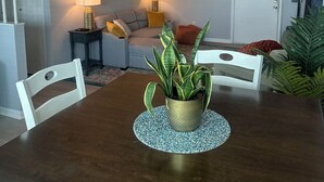 Un coin repas avec une table en bois foncé, des chaises blanches, un ventilateur de plafond et une plante en pot.