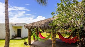 A thatched-roof structure with a hammock and a white building with a door. - Quintal de Areias (Santo Amaro do Maranhão)
