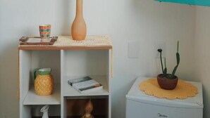 A small white cabinet with a shelf, a vase with dried flowers, a pineapple-shaped container, and a small potted plant on a white table. - Quintal de Areias (Santo Amaro do Maranhão)