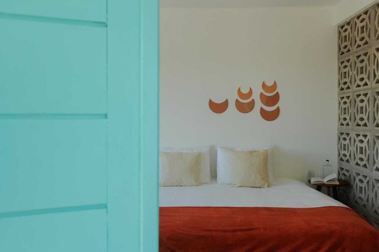 A bedroom with a bed, pillows, a red blanket, and a decorative wall with a geometric pattern.