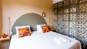 A hotel room with a large bed, decorative pillows, a wall with intricate cut-out patterns, and a small shelf with a vase. - Quintal de Areias (Santo Amaro do Maranhão)