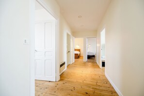 A hallway with wooden flooring leading to a bedroom with a bed and a bedside table. - Large Character Home (Binic-Étables-sur-Mer)