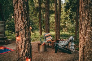 En campingplats i skogen med en metallspis, en grön stol och en filt.