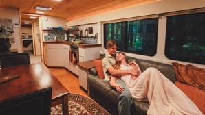 A cozy living room with a couch, a dining table, and a kitchen area. - Madrone Hideout-Artist Bus Retreat at Azalea Grove Getaway (Douglas County)