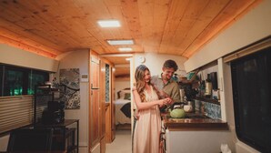 A kitchen with wooden ceiling, a dining area with a table and chairs, and a bedroom with a bed and window. - Madrone Hideout-Artist Bus Retreat at Azalea Grove Getaway (Douglas County)
