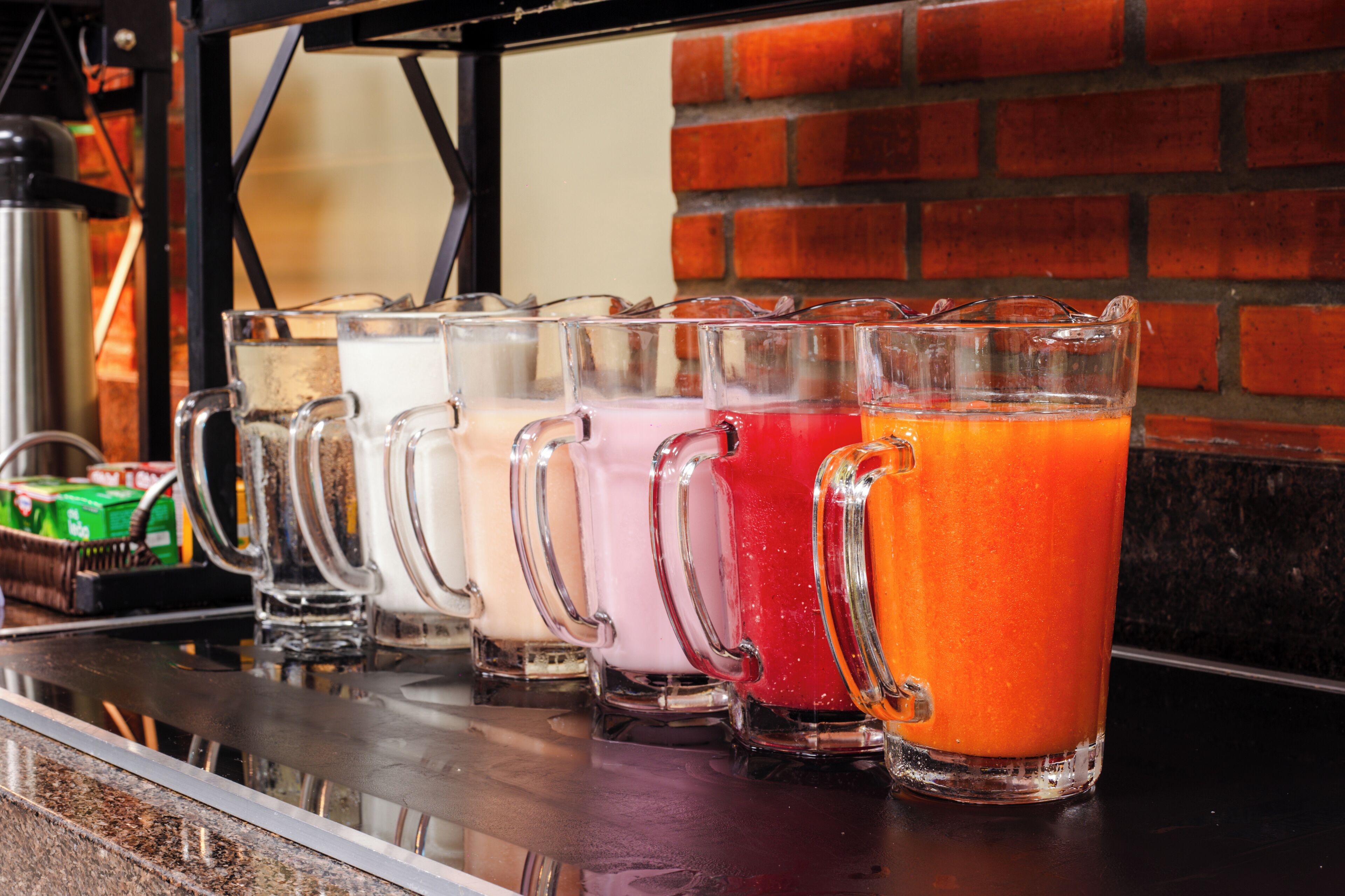 A row of clear glass mugs with different colored drinks on a bar counter.
