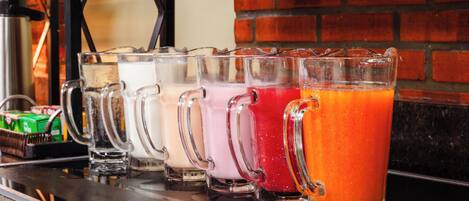 A row of clear glass mugs with different colored drinks on a bar counter.