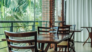 A dining area with wooden tables and chairs, large windows with a view of greenery, and a brick wall. - Rede Andrade Rio Branco (Rio Branco)