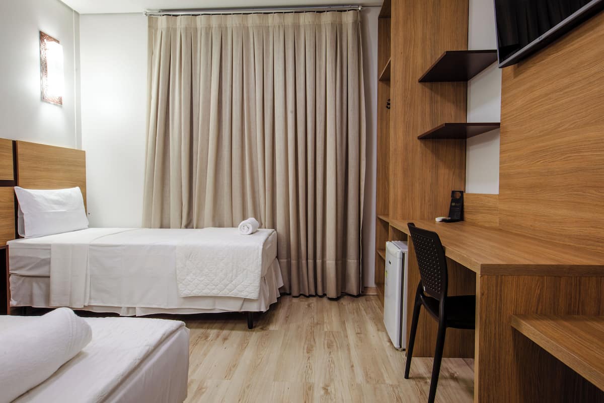 Ett hotellrum med två sängar, ett skrivbord, en stol och ett stort fönster med gardiner.