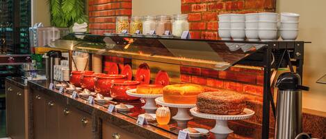 A buffet counter with various food items, a coffee machine, and a trash can.