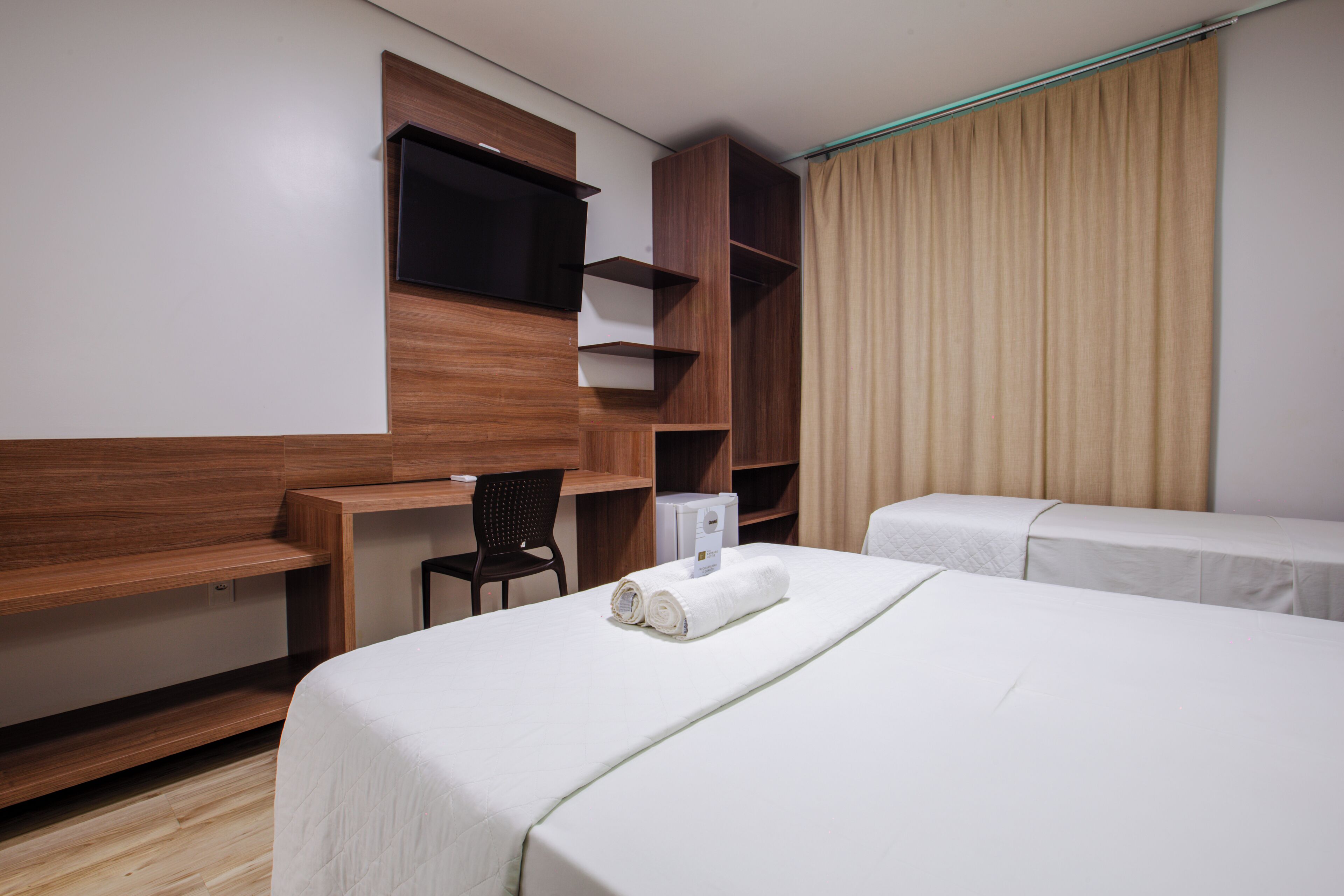 A hotel room with a bed, a desk, a chair, a TV, and a wardrobe.