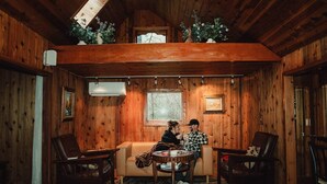 A cozy wooden cabin interior with a sofa, two chairs, a small table, and a window with a view of trees. - Blissful Solitude Cottage (Douglas County)