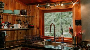 A wooden cabin kitchen with a large window, a sink, and various kitchen utensils. - Blissful Solitude Cottage (Douglas County)