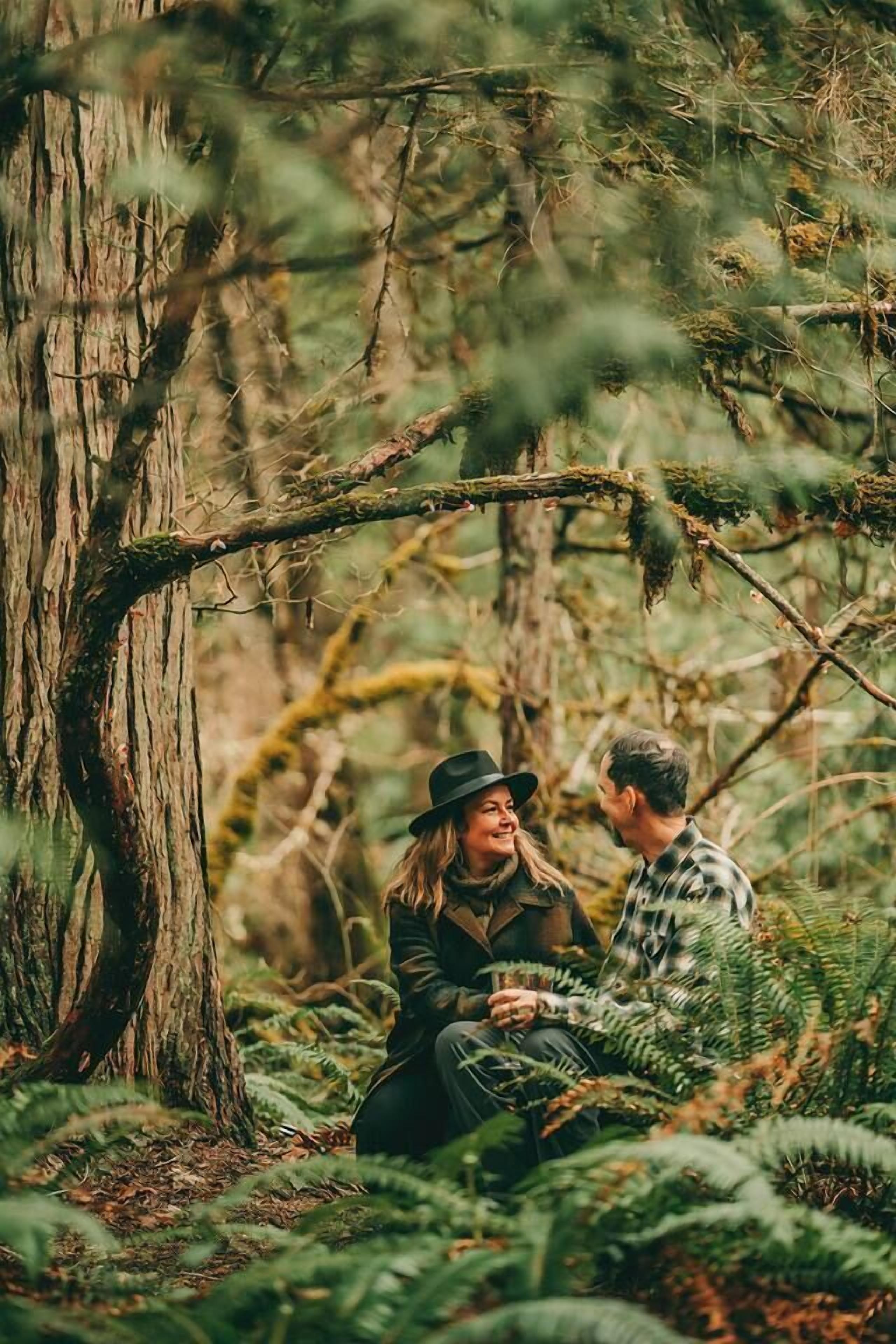 Un couple est assis sur le sol de la forêt, entouré d’arbres et de fougères.
