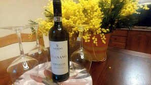 Una botella de vino Fugnano sobre una mesa, con un sacacorchos, rodeada de copas de vino y un arreglo floral amarillo.