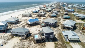 An aerial view of a coastal residential area with houses on stilts, some with attached decks and a swimming pool. - Sonny Daze~Private Heated Pool~Sleeps 12 (Dauphin Island)