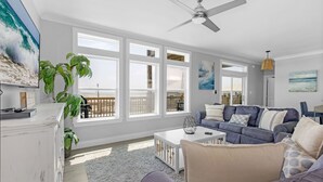 A spacious living room with a large window, a ceiling fan, a white coffee table, and a blue sofa. - Sonny Daze~Private Heated Pool~Sleeps 12 (Dauphin Island)