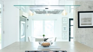 Una cocina moderna con campana de vidrio, armarios blancos y un comedor con mesa y sillas.