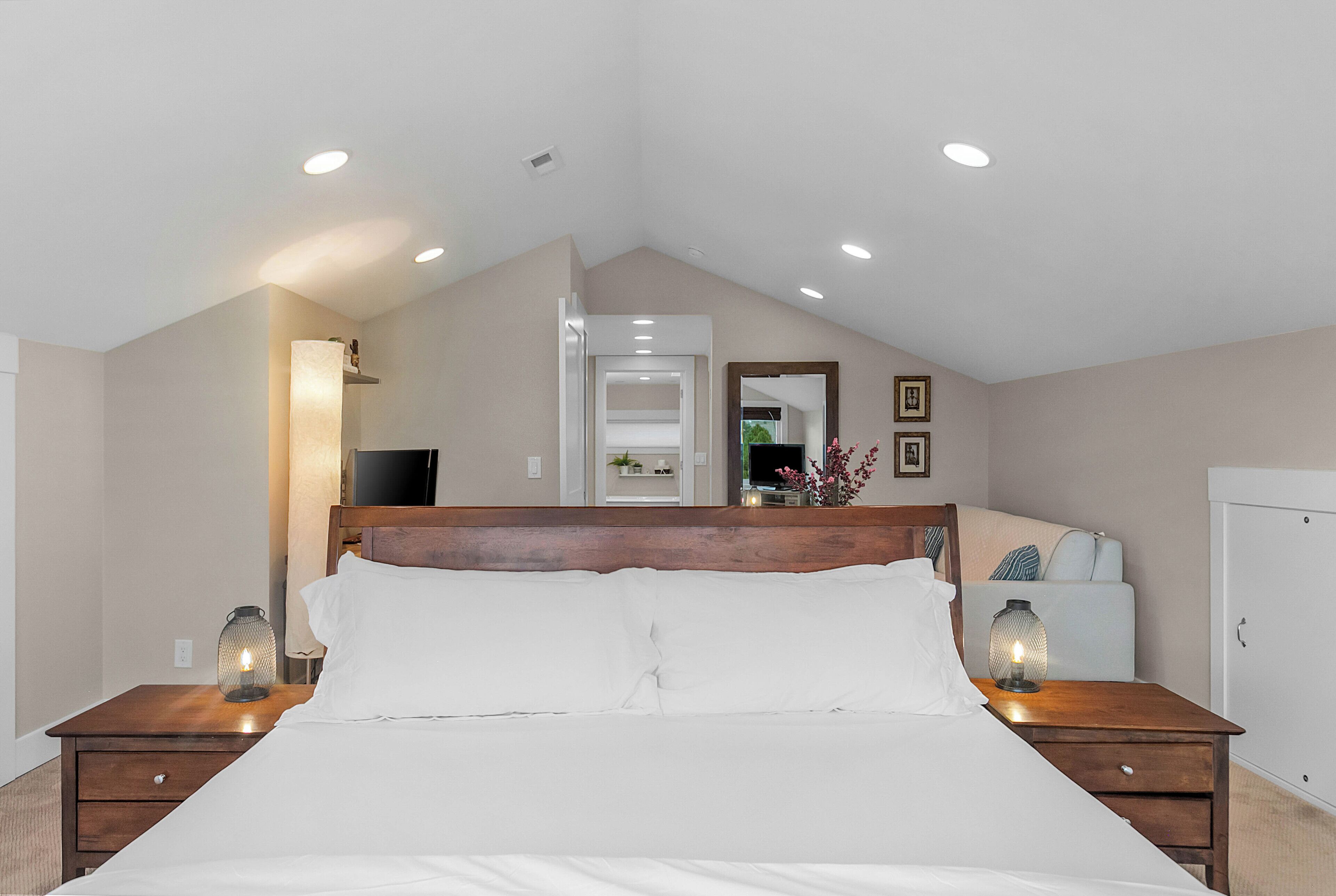 A bedroom with a bed, nightstands, a dresser, a mirror, and recessed ceiling lights.
