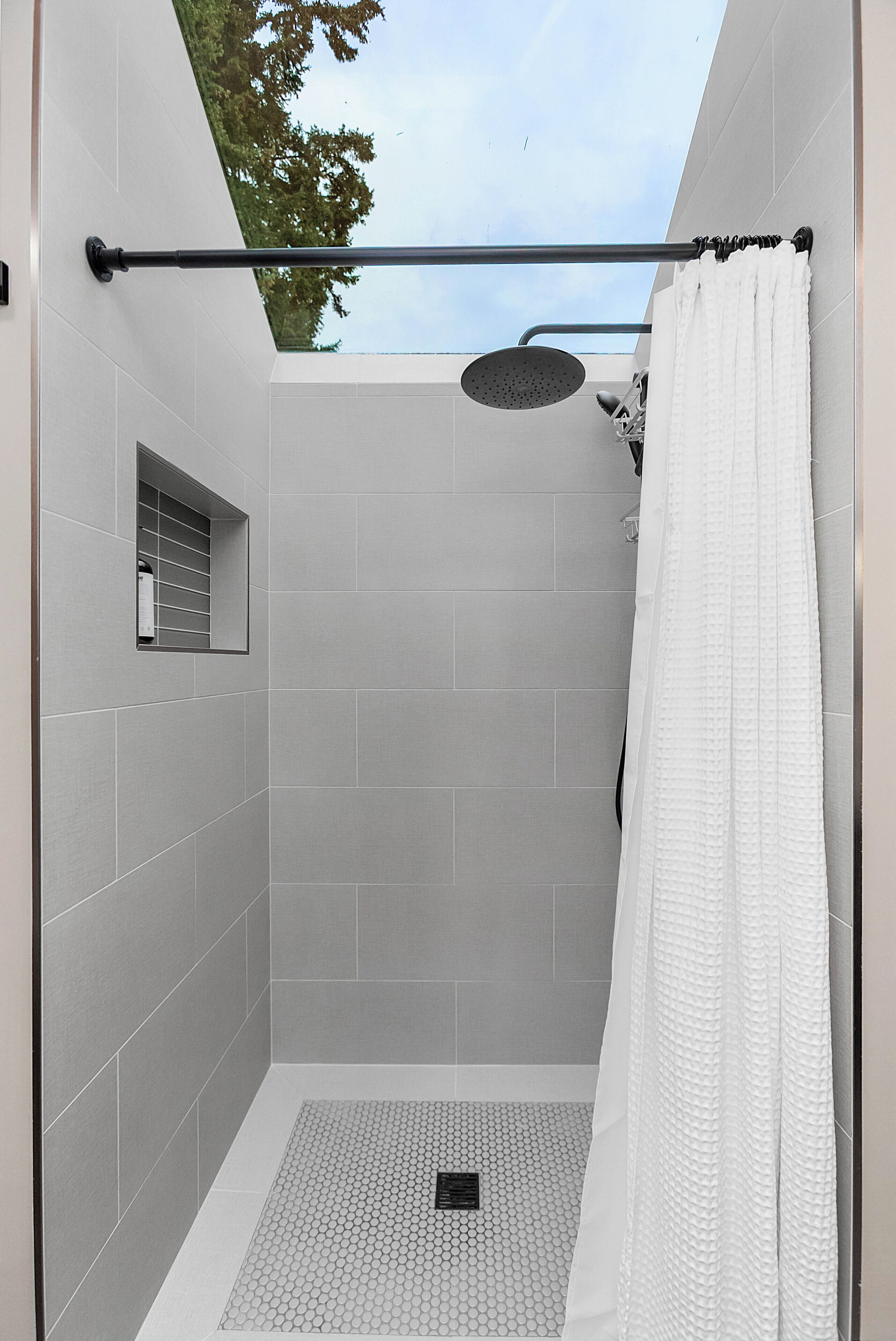 A modern shower area with grey tiles, a rain showerhead, and a white shower curtain.