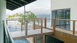 A modern building with a wooden deck and a glass balcony overlooking a body of water. - Casa de Frente pro Mar com Piscina (Palhoca)