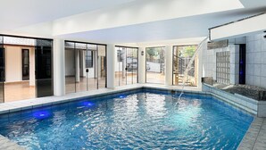 An indoor swimming pool with clear blue water, surrounded by glass doors and a tiled floor. - Casa de Frente pro Mar com Piscina (Palhoca)