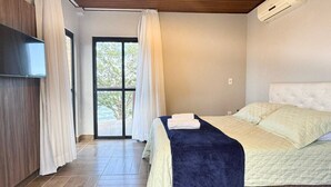 A bedroom with a bed, a TV mounted on the wall, and a sliding glass door leading to an outdoor area. - Casa de Frente pro Mar com Piscina (Palhoca)