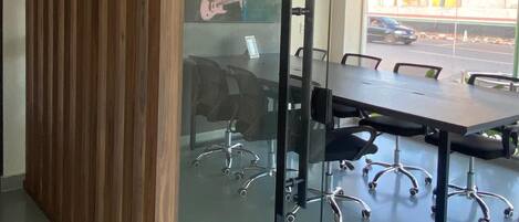 A modern meeting room with a glass partition, a wooden panel, and a large table with office chairs.