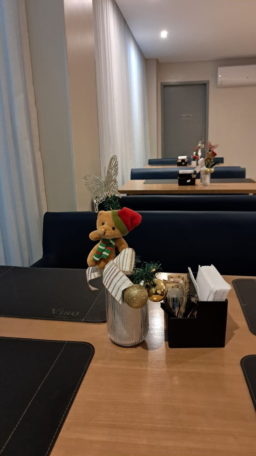 Una habitación de hotel acogedora con un sofá mullido, una mesita con un osito de peluche, un florero con una planta y una bandeja negra con bolígrafos.