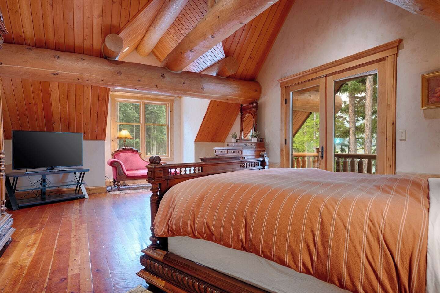 Un dormitorio amplio con una cama grande, un televisor y un aparador de madera. Hay un balcón con vista a árboles.