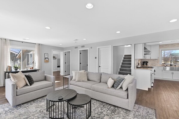 A modern living room with a grey sofa, two round coffee tables, and a staircase leading to a kitchen. - Charming 3-bedroom lake house in Waterford with amazing views (Waterford)