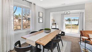 Un comedor con mesa de madera, sillas negras y vista a un lago a través de amplios ventanales.
