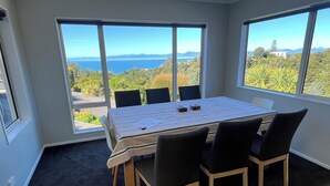 A room with a large table and chairs, large windows with a view of the sea and greenery.