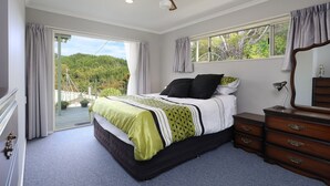 A bedroom with a bed, a dresser, a ceiling fan, and a view of greenery outside.