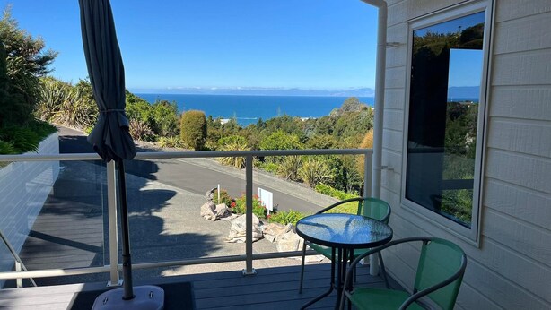 A balcony with a view of the ocean, a table, and chairs.