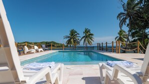 Un espace piscine doté de chaises longues blanches et offrant une vue dégagée sur l’océan.