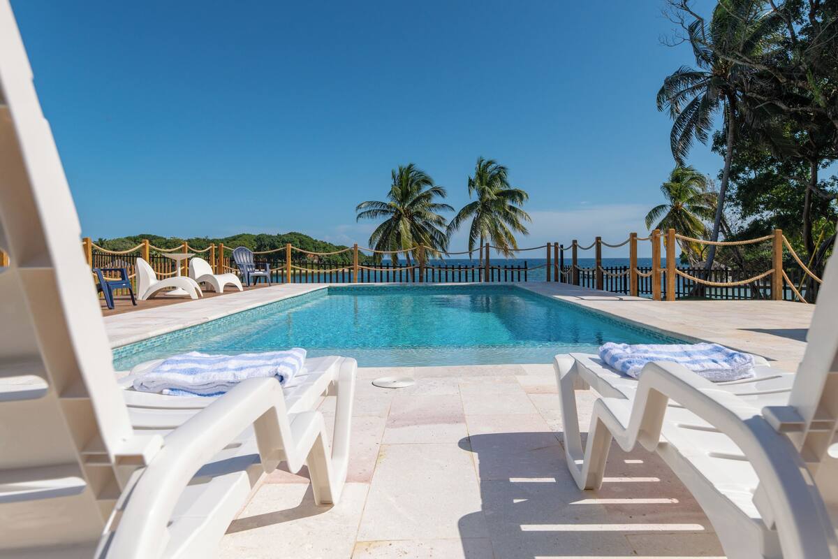 A pool area with white lounge chairs and a clear view of the ocean.