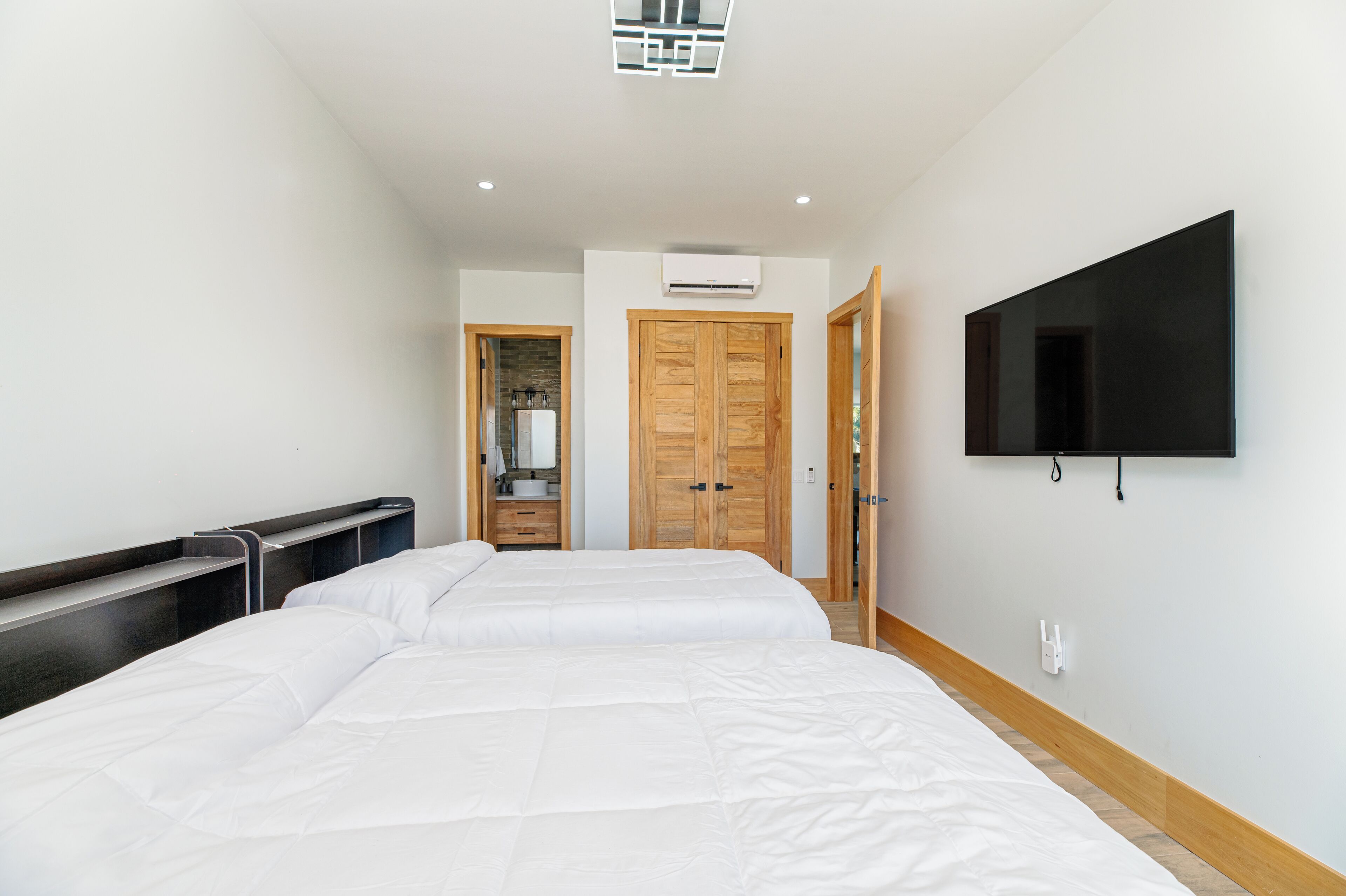 A hotel room with two beds, a TV mounted on the wall, and a wooden wardrobe.