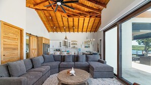 Un salon moderne avec un grand canapé d’angle, une table basse ronde et un ventilateur de plafond.