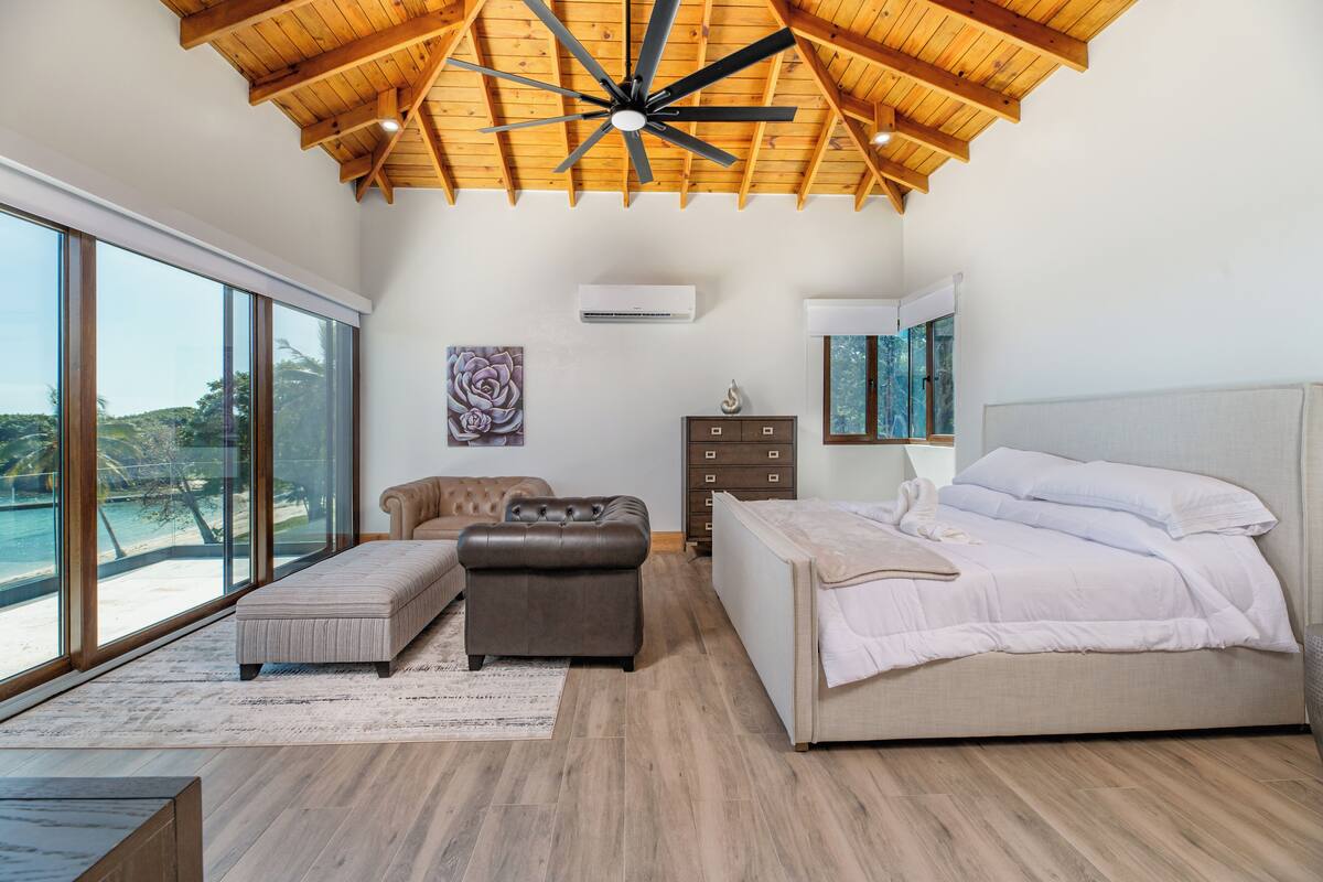 A bedroom with a large bed, a bench, a dresser, and a ceiling fan.