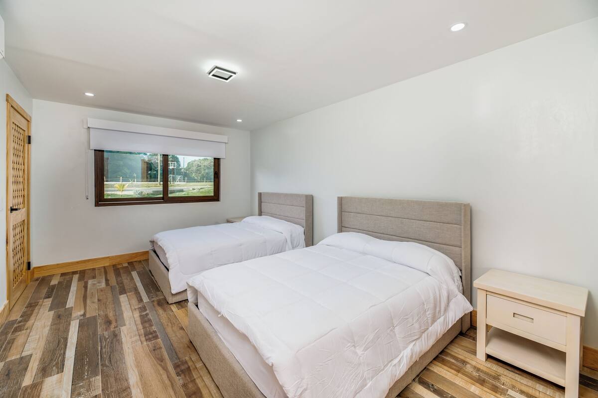 A bedroom with two beds, a window with a view, and a wooden floor.
