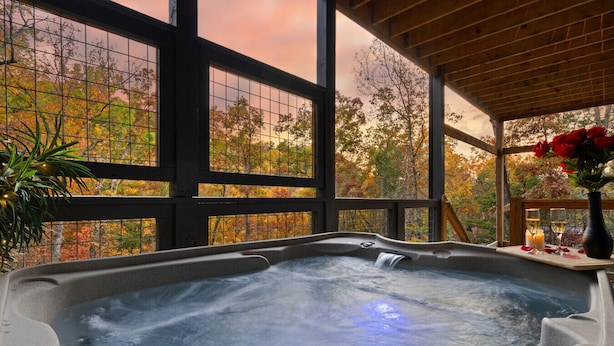 Ein Whirlpool mit Holzterrasse und Glasumrandung, umgeben von Herbstlaub.