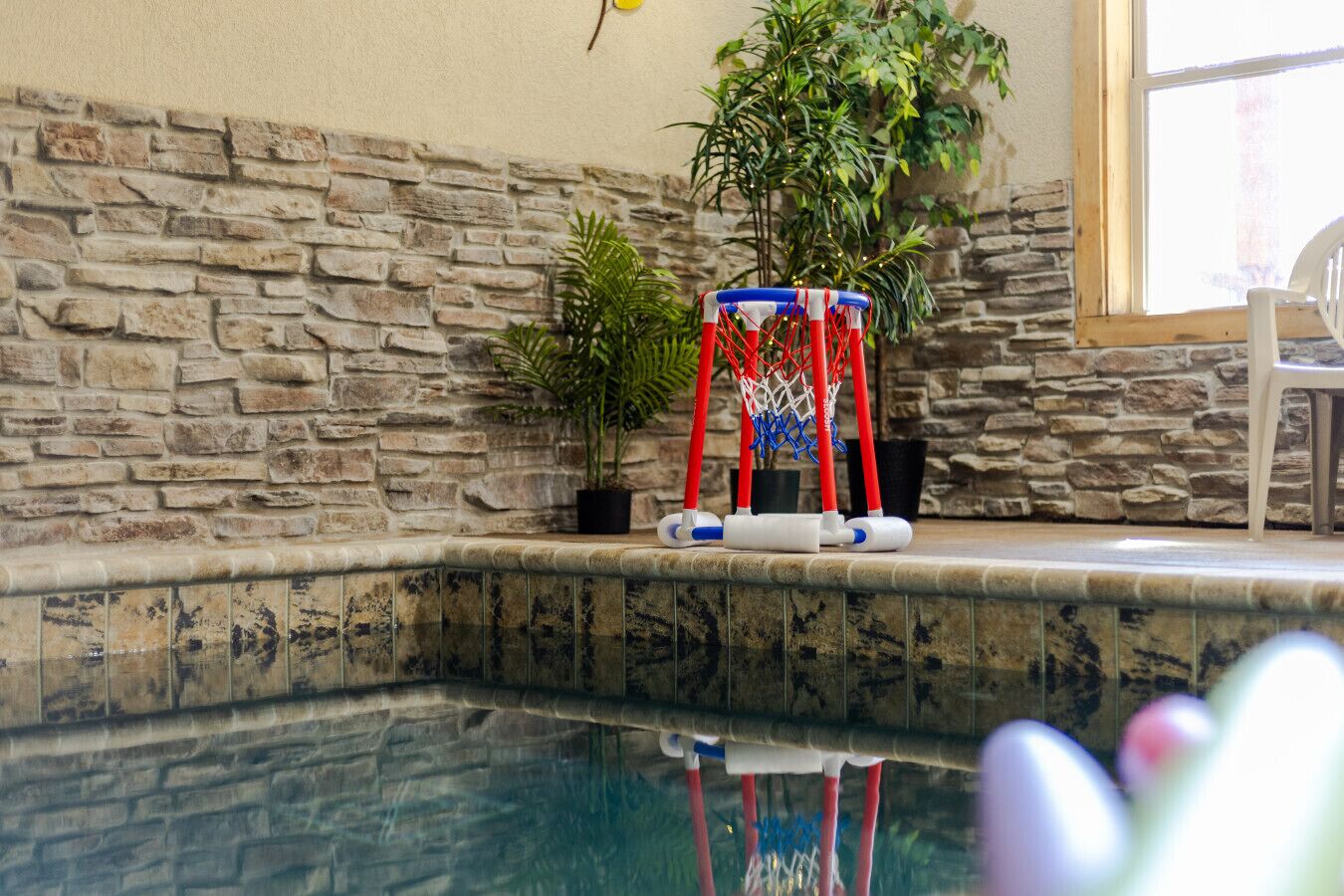 A pool area with a stone wall, a basketball hoop, and a potted plant.