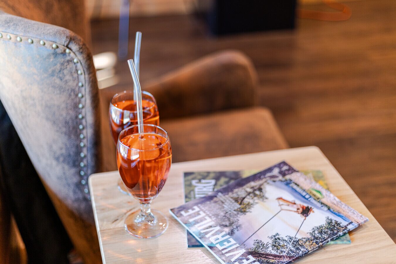 Two glasses of amber-colored beverage on a wooden table with a magazine.