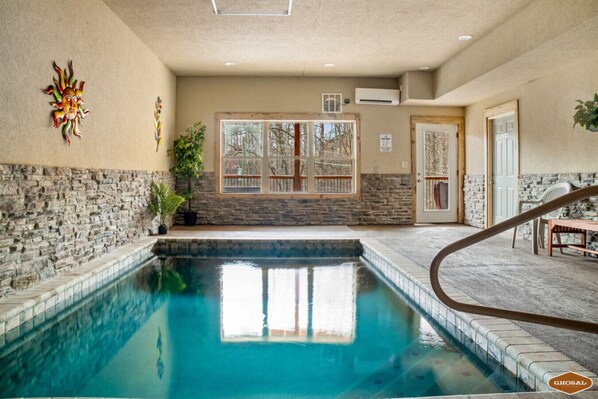 A pool area with stone walls, a wooden deck, and a staircase leading to a door.